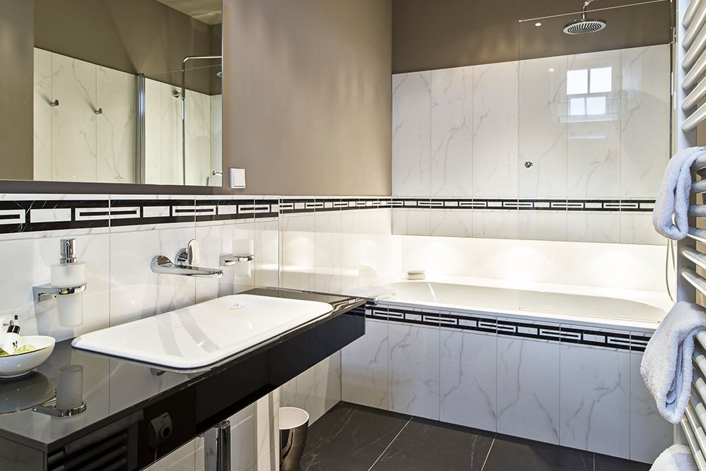 Modernes Badezimmer mit großer weißer Badewanne, schwarzem Aufsatzwaschbecken und grau gefliestem Boden. Die Wände sind mit weißen und schwarzen Fliesenakzenten versehen.