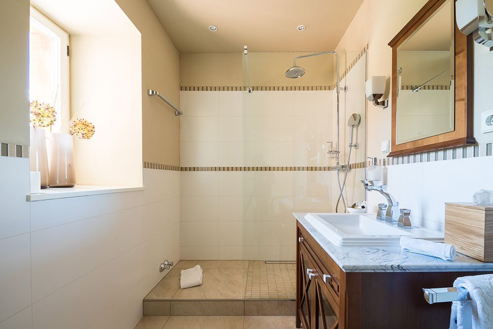 Modernes Badezimmer mit ebenerdiger Dusche, großem Spiegel und Waschbecken. Natürliches Licht durch ein Fenster erhellt den Raum.