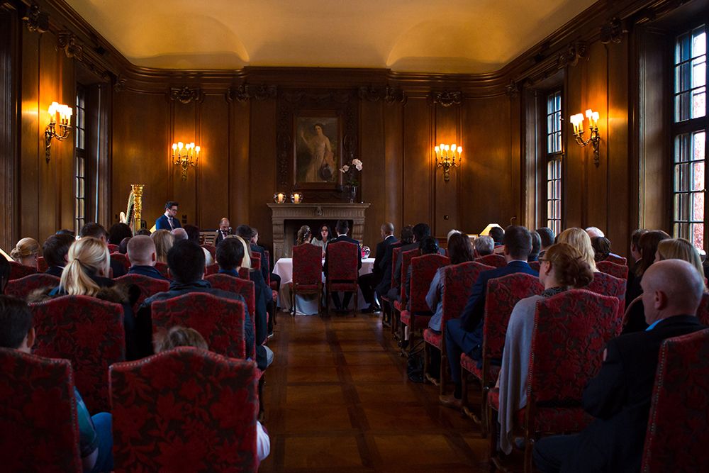 Menschen sitzen in einem schwach beleuchteten Raum mit Holzvertäfelung und hören den Vortragenden an einem Tisch vorne zu, als würden sie einer märchenhaften Erzählstunde in einem eleganten Schloss beiwohnen.