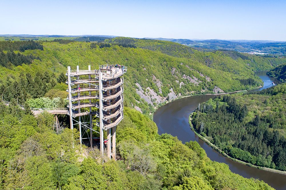 Aerial view of a spiral observation tower near a hotel surrounded by lush green forest and a winding river - perfect for day trips and other exciting activities.