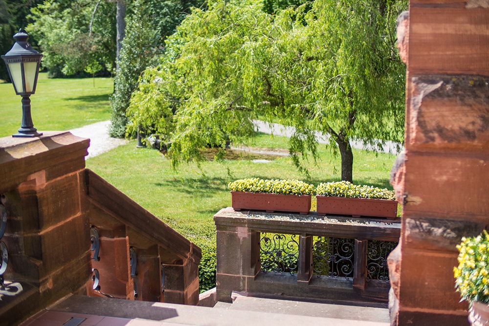 Eine Steintreppe mit Blumenkästen führt zu einem üppigen Garten mit Bäumen und einer Straßenlaterne.