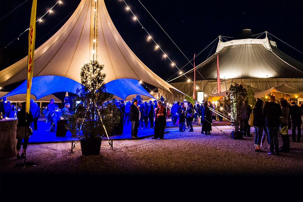 Im Schein der Lichterketten treffen sich die Menschen zu den Kammermusiktagen, umgeben von üppigen Pflanzen und beleuchteten Zelten. Die nächtliche Atmosphäre wird durch Kultur und Musik bereichert und schafft ein unvergessliches Erlebnis.