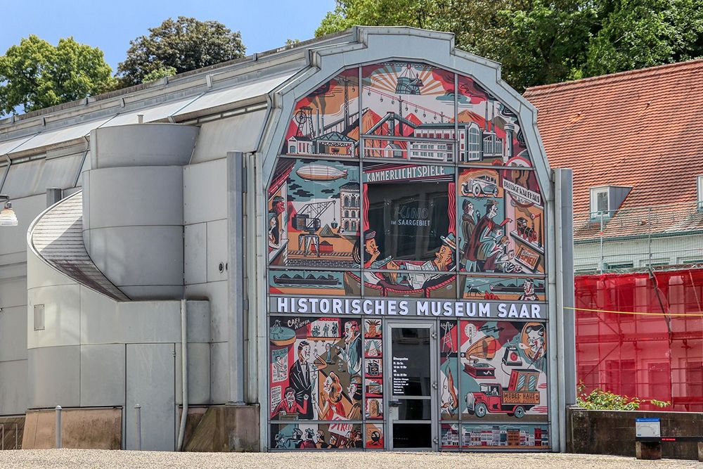 Entrance to the Saar Historical Museum with colourful mural and signage, surrounded by trees and adjacent buildings.