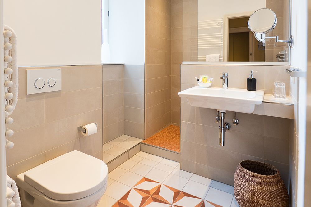 Modernes Badezimmer mit gefliesten Wänden, ebenerdiger Dusche, wandmontiertem Waschbecken, Toilette und Weidenkorb auf dem Boden.
