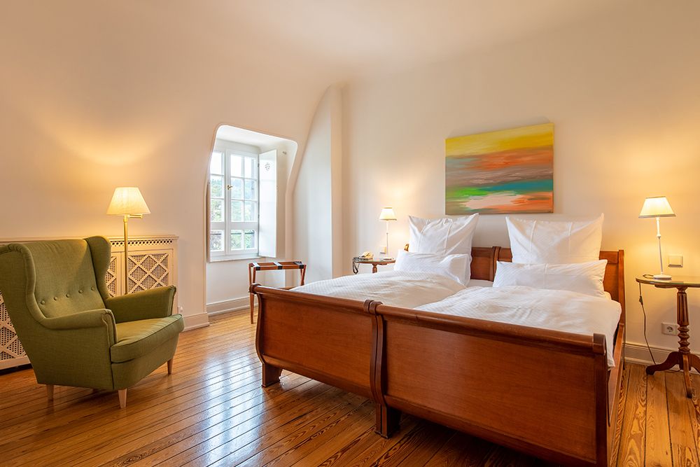 Ein gemütliches Schlafzimmer mit zwei Holzbetten, einem Sessel, drei Lampen und einem bunten Gemälde an der Wand.