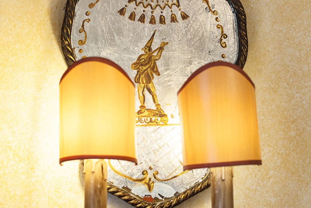 Zwei Lampen mit beigen Schirmen stehen vor einem raumprägenden Wanddekor mit einem goldenen Trompete spielenden Clown und schaffen eine stimmungsvolle Atmosphäre.