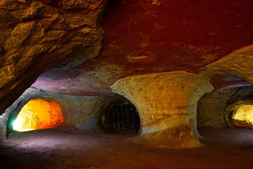 Spacious underground cave with textured stone ceiling and bright orange and yellow light reflecting off the walls and floor.