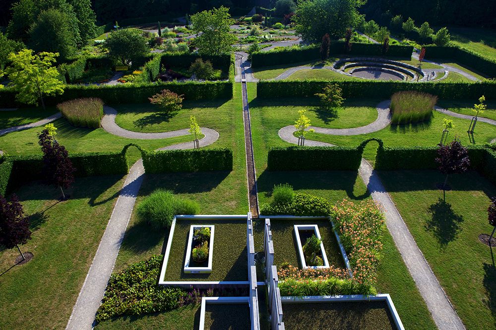 Aerial view of a formal garden with symmetrical pathways, lush greenery and a circular patterned section, perfect for those seeking hotel proximity and charming day trips.