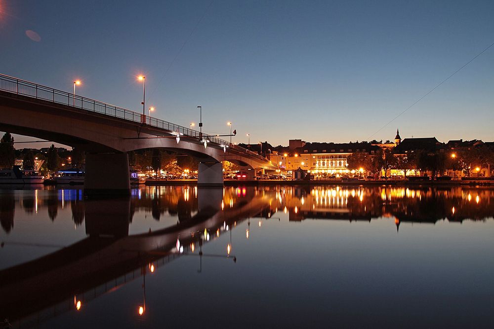 Bridge over a calm river at dusk, city lights reflected in the water.