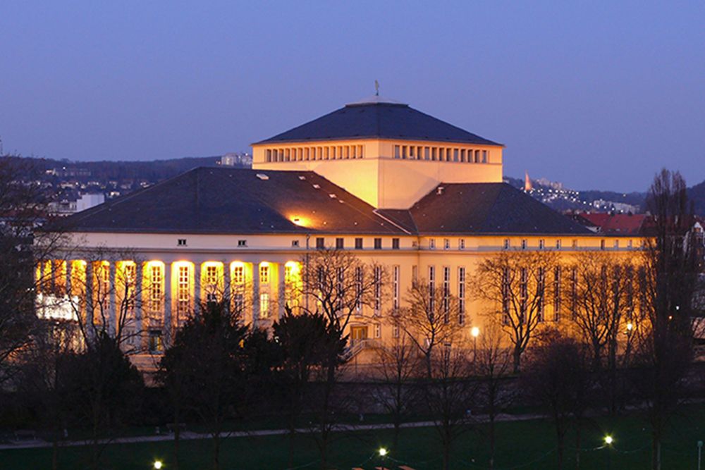 Ein beleuchtetes Gebäude mit sechseckigem Dach erhebt sich majestätisch vor dem Abendhimmel. Die ruhige Szene wird von den umliegenden Bäumen wunderschön eingerahmt und schafft einen malerischen Moment.