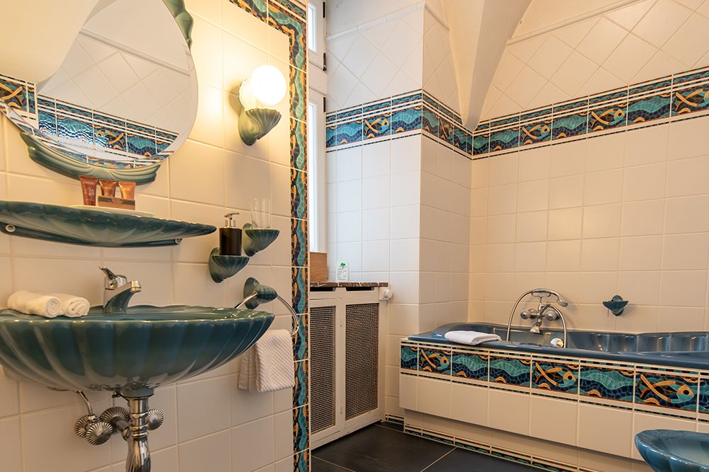 Gefliestes Badezimmer mit blauem Waschbecken und passender Badewanne, Wandspiegel und dekorativen blauen und orangefarbenen Zierleisten.