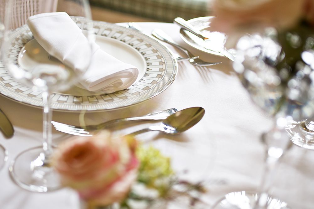 Elegante Tischdekoration für ein privates Abendessen zu zweit, mit einem Teller und einer gefalteten Serviette, umgeben von Besteck und Gläsern. Sanft verschwommene Blumen im Vordergrund sorgen für eine intime Atmosphäre.